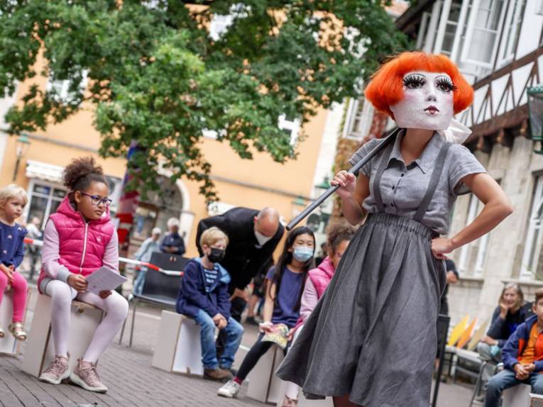 Kinder auf dem Ballhofplatz betrachten eine maskierte Schauspielerin.